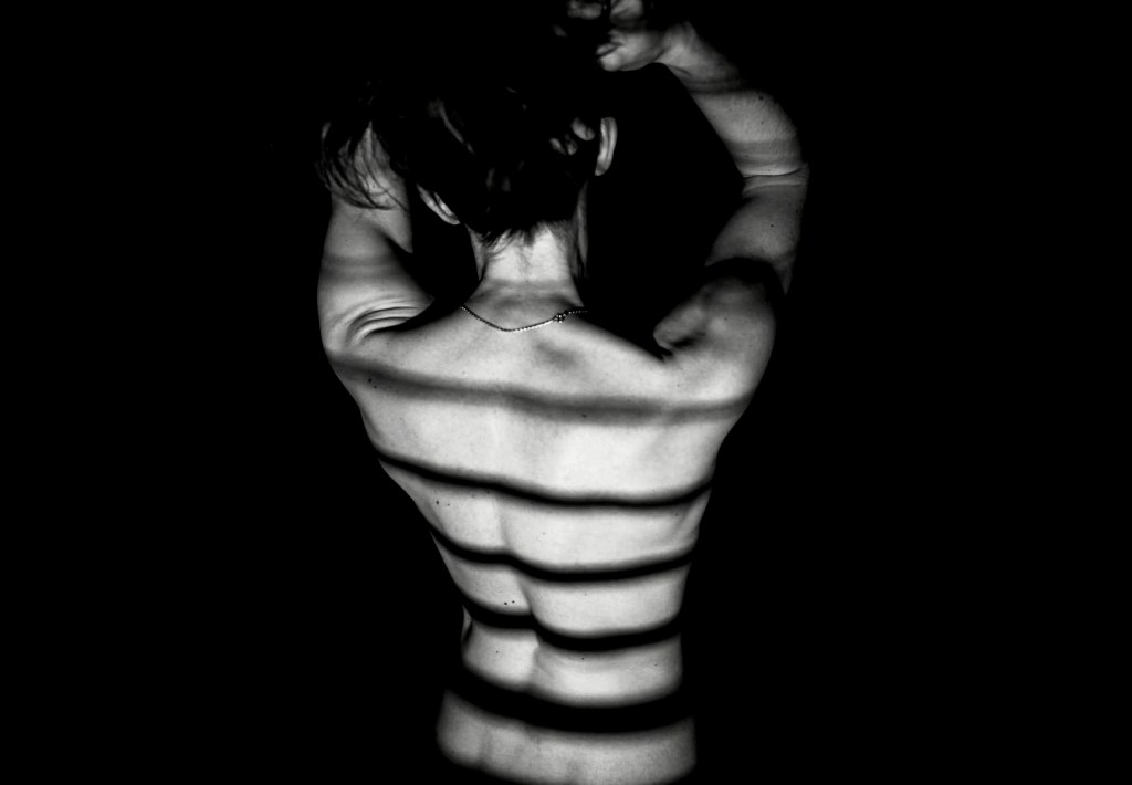 Photographie en noir et blanc d'un corps enveloppé de lumière et d'ombres projetées